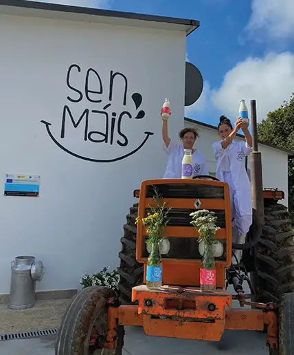 Marta y Ana sobre un tractor con botellas de leche en la mano